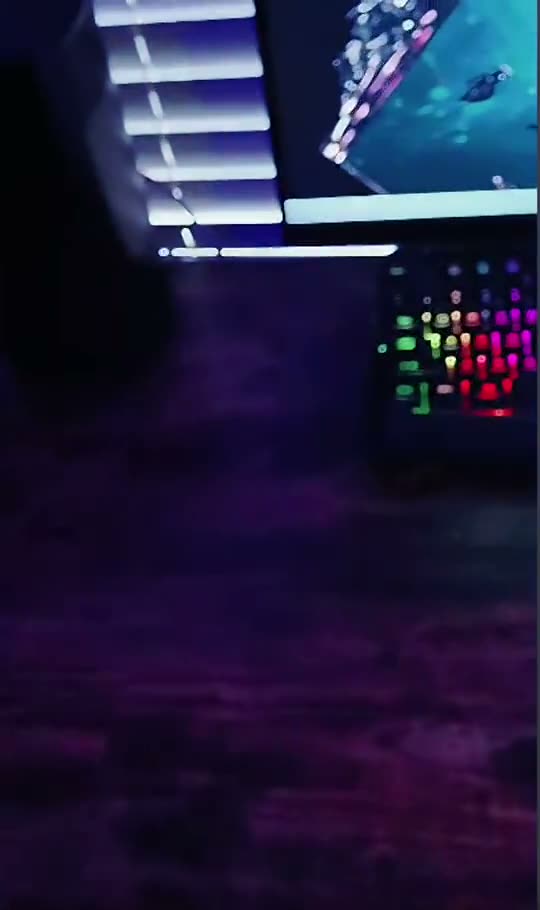 A desk setup with an RGB keyboard, monitor and tower lit blue and pink.
