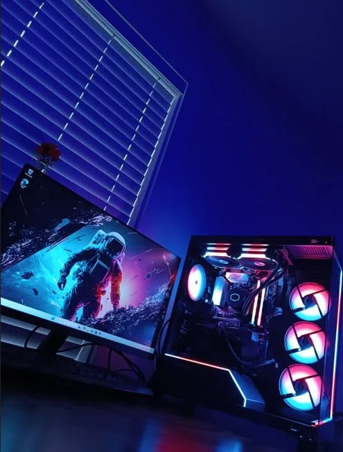 A finished build glowing pink and blue beside a monitor in a dark, blue-lit room.